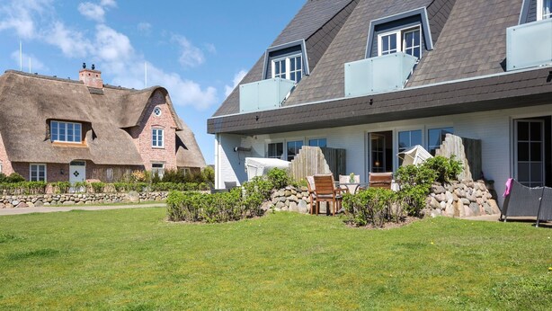 A residential area with a grassy lawn, a stone wall, and two houses with distinct architectural styles. - Sylter Refugium, App. 2 - Mitten im Beliebten Inselort Wenningstedt Befindet Sich Dieses Appartement (Wenningstedt-Braderup (Sylt))