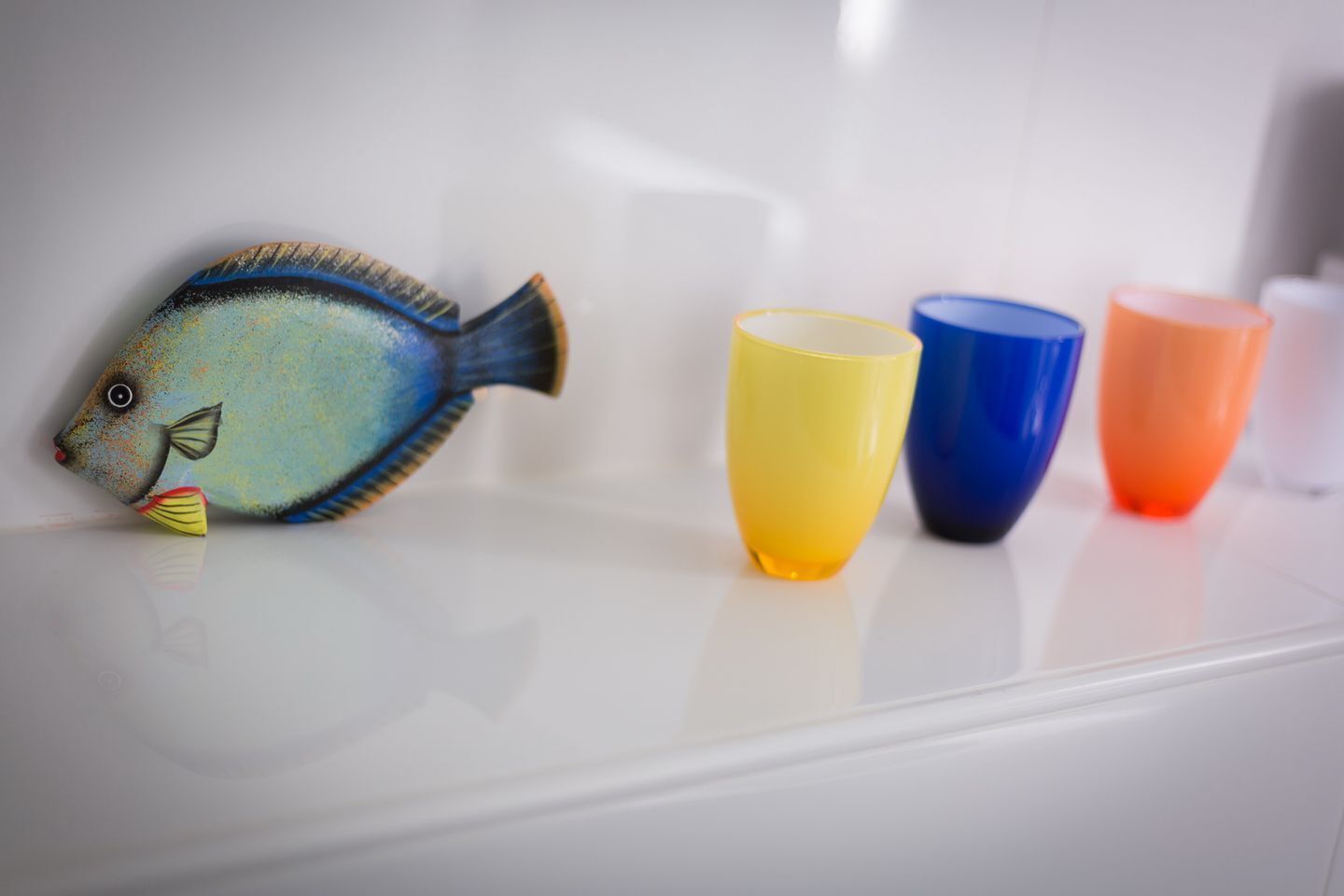 A fish-shaped object on a white surface with four colorful cups beside it.