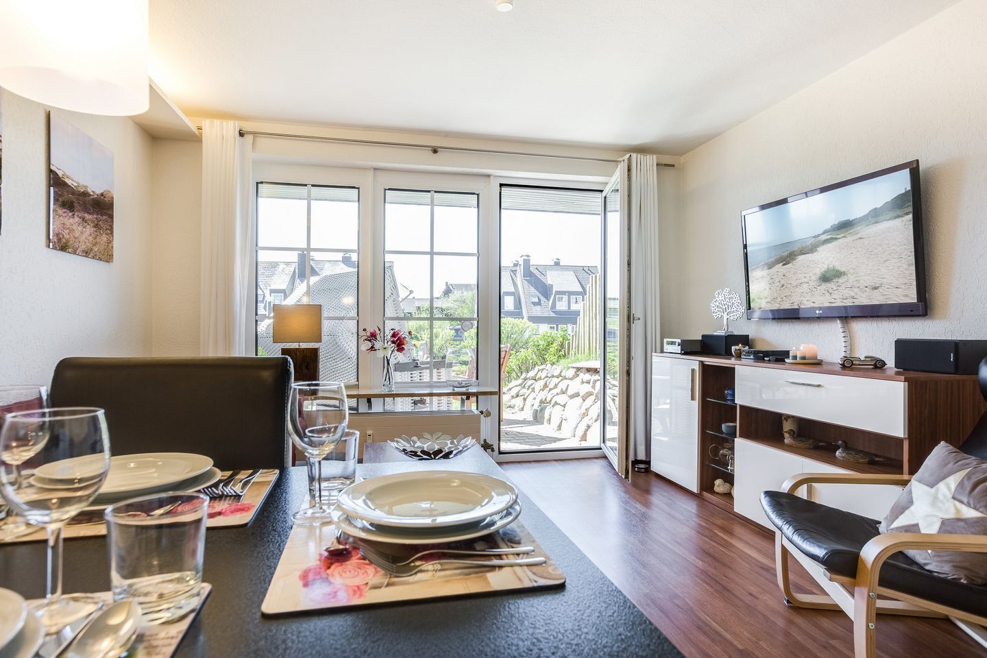 Un coin repas avec une table dressée pour quatre personnes, un téléviseur fixé au mur et une vue sur l’extérieur grâce à une porte vitrée.