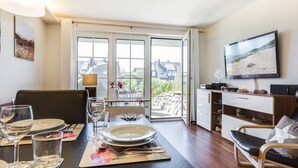 A dining area with a table set for four, a television mounted on the wall, and a view of the outside through a glass door. - Sylter Refugium, App. 2 - Mitten im Beliebten Inselort Wenningstedt Befindet Sich Dieses Appartement (Wenningstedt-Braderup (Sylt))