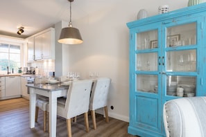 A dining area with a white table set for four, a blue cabinet with glass doors, and a hanging light fixture.