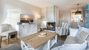 A modern living room with a fireplace, a television, and a dining area with striped chairs. - Ameland, App. 12 - Charme & Luxus Zwischen Dorfteich und Golfplatz (Wenningstedt-Braderup (Sylt))