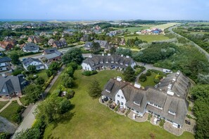 An aerial view of a residential area with houses, a large grassy field, and a river in the background. - Ameland, App. 12 - Charme & Luxus Zwischen Dorfteich und Golfplatz (Wenningstedt-Braderup (Sylt))