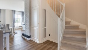 A spacious living area with a wooden staircase, a white fireplace, and a dining area with a table and chairs. - Ameland, App. 12 - Charme & Luxus Zwischen Dorfteich und Golfplatz (Wenningstedt-Braderup (Sylt))