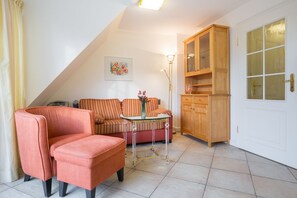 Ein Wohnzimmer mit einer Couch, einem kleinen Tisch mit Blumen, einem Schrank und einer Tür mit Milchglasfenstern.