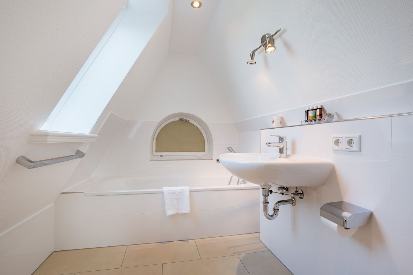 Un baño moderno con tragaluz, una bañera independiente, un lavabo de pared y un perchero para toallas.