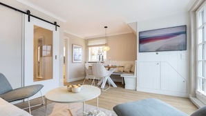 Un salon moderne comprenant un canapé, une table à manger avec des chaises, un téléviseur fixé au mur et une porte coulissante donnant sur une autre pièce.