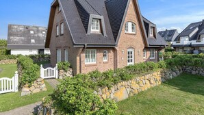 Une maison à deux étages, dotée d’un toit à forte pente, d’une façade en briques et d’un mur de soutènement en pierre.