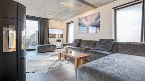 A modern living room with a large grey sofa, a wooden coffee table, and a black fireplace. - Willms Living, Long Beach House - Design-avantgarde. Viel Raum. Direkt an den Tinnumer Wiesen (Sylt)