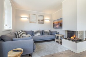 Una sala de estar moderna con un sofá gris, almohadones a rayas, una alfombra blanca, una pequeña mesa de madera y una chimenea.