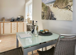 A modern kitchen with a glass table, a bottle of wine, and a bowl of fruit. - Zita, App.8 - Dorfteich. Dünen. Erholung (Wenningstedt-Braderup (Sylt))