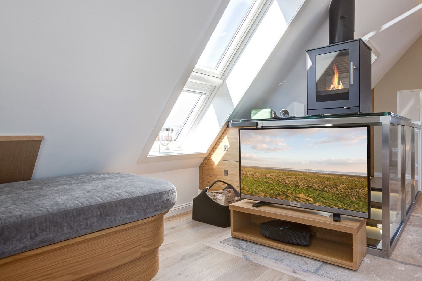A loft bedroom with a skylight, a bed, a TV, and a wood-burning stove.