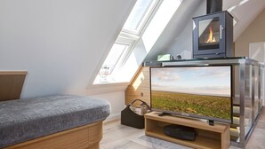 A loft bedroom with a skylight, a bed, a TV, and a wood-burning stove. - Willms Living, Sky - Design [&] Stil Pur. Raumwunder für Individualisten an den Tinnumer Wiesen (Sylt-Ost)