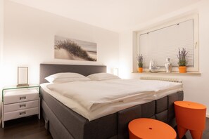 A bedroom with a bed, bedside tables, a window with blinds, and a painting on the wall. - Westerbrise, App. 2 Studio Veit - Studio Veit - Ruhige Lage in Wenningstedt Zwischen Dorfteich und (Wenningstedt-Braderup (Sylt))