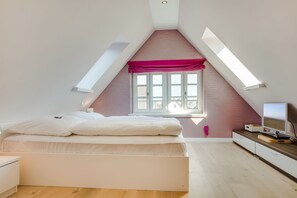 Et soveværelse med skråvæg, seng, et vindue og et fjernsyn.