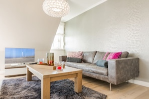En moderne stue med en grå sofa, et træsofabord og et fjernsyn på et stativ.