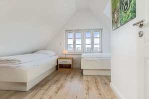 Een kleine, witte slaapkamer in de zolderstijl met twee bedden, een nachtkastje en een raam met uitzicht.