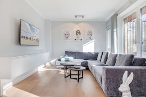 Uma sala de estar moderna com um sofá modular cinza, uma mesa de centro redonda e uma TV de tela plana na parede.