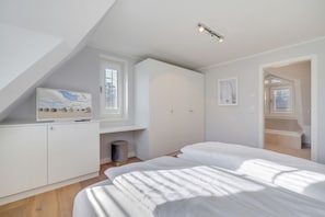 Quarto moderno com teto inclinado, uma janela grande, televisão e uma cama.