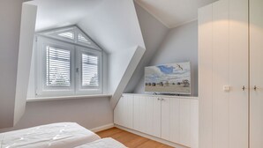 Un dormitorio con techo inclinado, una ventana con persianas, un televisor sobre un mueble y dos camas.