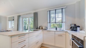 Una cocina moderna con armarios blancos, una isla grande con un fregadero y una ventana con persianas.
