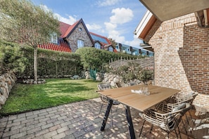 Un espace patio aménagé avec une table et des chaises, un mur en pierre et une vue sur un bâtiment doté d’un toit rouge.