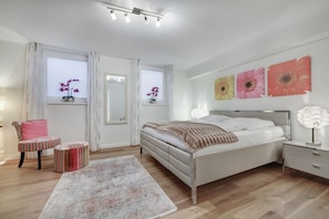 Une chambre à coucher moderne, avec un lit, des tables de chevet, une chaise, un tapis et des œuvres d’art accrochées aux murs.