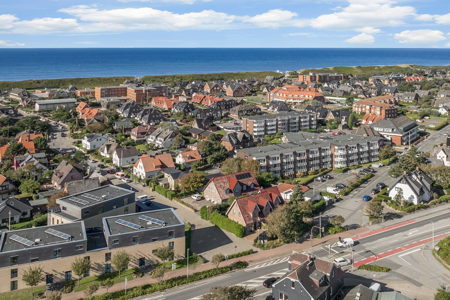 A coastal town with a mix of traditional and modern buildings, including a prominent red-roofed building and a modern structure with solar panels.