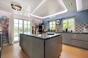 Una cocina moderna con una isla grande, iluminación colgante y vistas a la vegetación exterior.