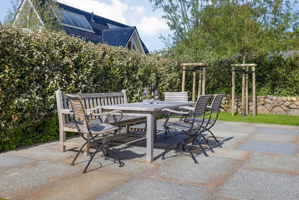 Un patio al aire libre con una mesa y sillas de madera, rodeado de baldosas de piedra.