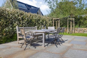 An outdoor patio with a wooden table and chairs, surrounded by stone tiles.