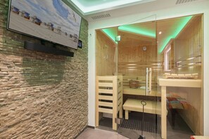 Un sauna avec des bancs en bois, une porte en verre et un mur en pierre.