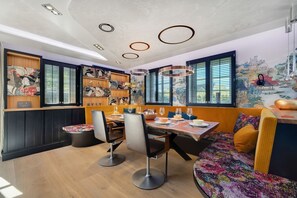 A restaurant with a wooden table, chairs, and a bench. There are shelves with artwork and a mural on the wall.