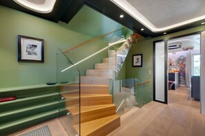 A modern staircase with glass railings, wooden steps, and a green wall with framed pictures.
