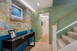 Un pasillo con un mural colorido, una consola con una fotografía enmarco y una escalera de madera.