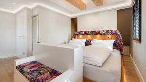 Una camera da letto con un letto, un piccolo angolo relax, travi in legno al soffitto e una finestra con persiane.