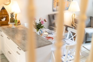 Una cocina moderna con una isla central, muebles blancos y un comedor con sofá gris y sillas blancas.