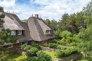 Et traditionelt hus med stråtækt tag, have og stenvægge.