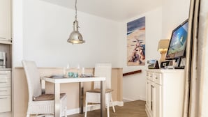 A dining area with a white table, wicker chairs, and a hanging pendant light. - Haus Am Dorfteich, App. 2 - 2-raum-appartement im Erd- und Untergeschoss mit ca. 40m² Nutzfläche (Wenningstedt-Braderup (Sylt))