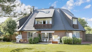 A two-story house with a sloped roof, a balcony, and a front porch with outdoor seating. - Haus Am Dorfteich, App. 2 - 2-raum-appartement im Erd- und Untergeschoss mit ca. 40m² Nutzfläche (Wenningstedt-Braderup (Sylt))