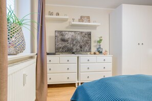 A bedroom with a bed, a dresser, a television, and a window with a plant. - Haus Am Dorfteich, App. Élise - Idylle & Komfort Unmittelbar am Dorfteich (Wenningstedt-Braderup (Sylt))