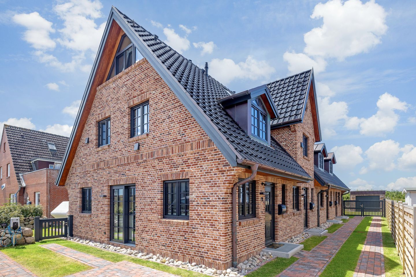 Une maison moderne à deux étages, avec une façade en briques, de grandes fenêtres et un toit en pente.
