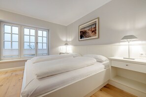Un dormitorio con una cama grande, una mesita de noche con lámpara, una ventana con persianas y un cuadro enmarcado en la pared.