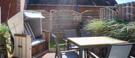 An outdoor patio with a table and chairs, a cushioned seating area, and a wooden fence.