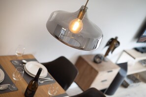 Ein Essbereich mit Tisch für zwei Personen, ausgestattet mit einer modernen Pendelleuchte, Weingläsern und Tellern.