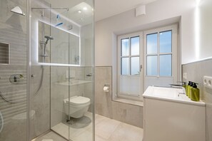 Un baño moderno con ducha envuelta en vidrio, inodoro y lavamanos con artículos de aseo.
