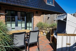 Un patio al aire libre con mesa y sillas de madera, un muro de ladrillo y una zona de estar cubierta.