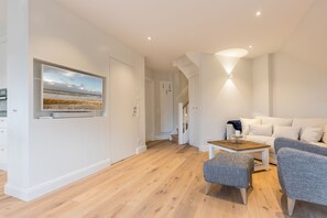 Un salon moderne avec un plancher en bois, un canapé blanc, un fauteuil gris et une table basse.