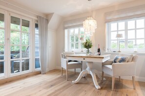A bright dining room with a wooden table, white chairs, and a chandelier.