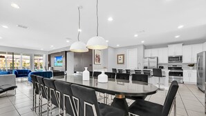 A modern kitchen with white cabinets, stainless steel appliances, and a dining area with a glass table and black chairs. - 8BR Modern Villa • Games&Movie Room • Near Disney (Kissimmee)